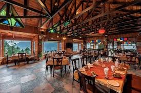 A cozy restaurant with wooden interiors, large windows offering scenic mountain views, and beautifully set dining tables, creating a warm and inviting atmosphere.